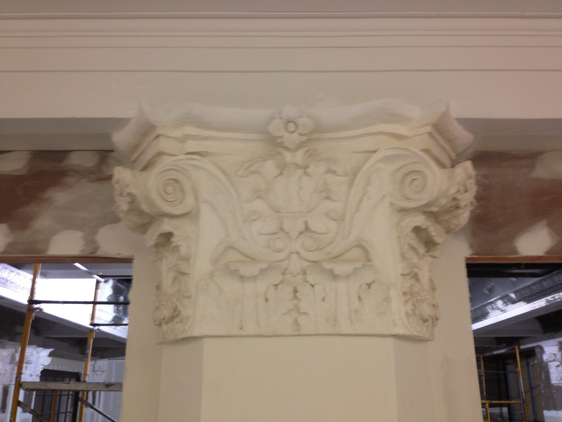 Ornate decorative plaster column capital during interior renovation with scaffolding