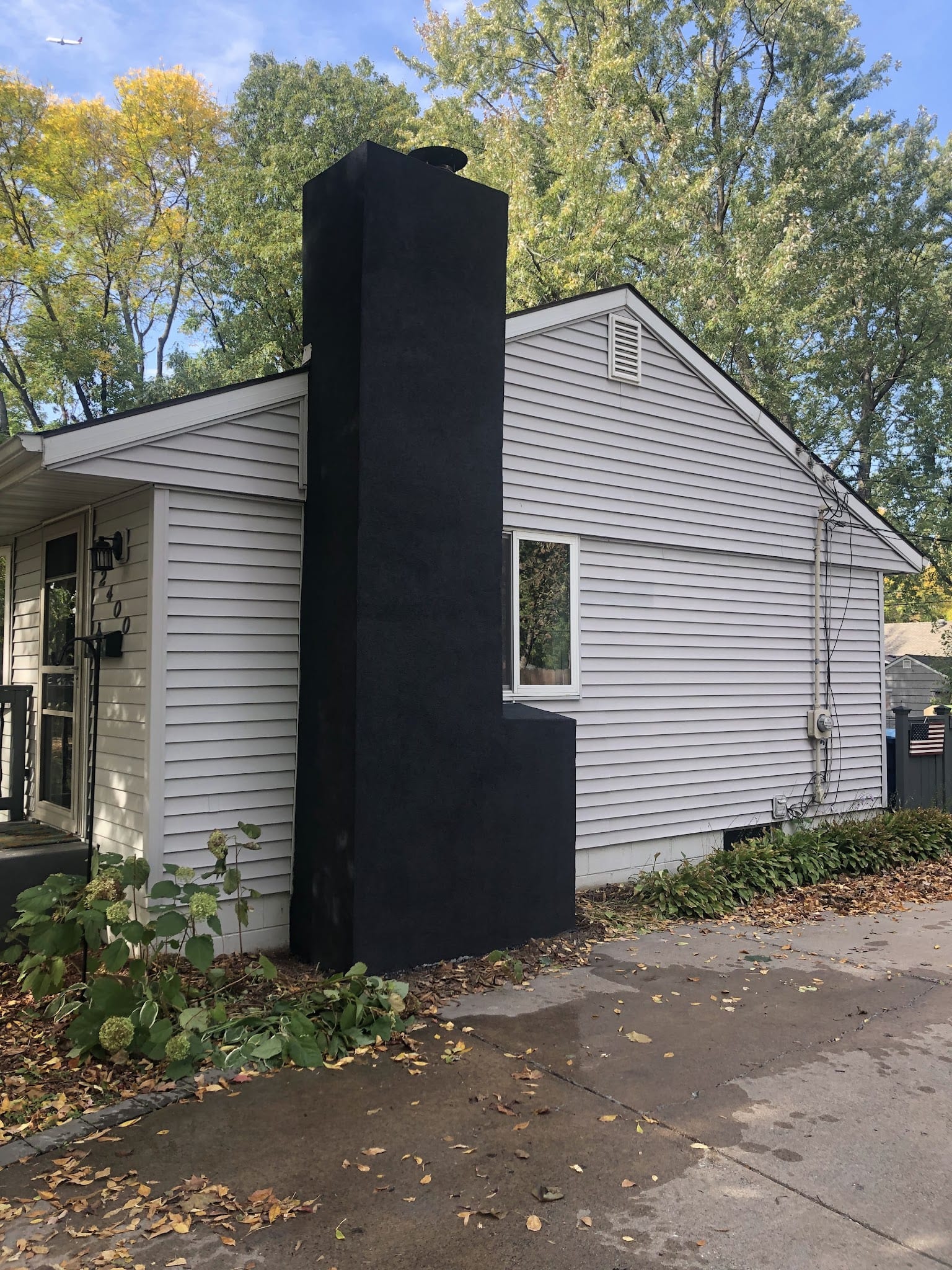 Black stucco chimney and base on gray vinyl-sided home exterior.