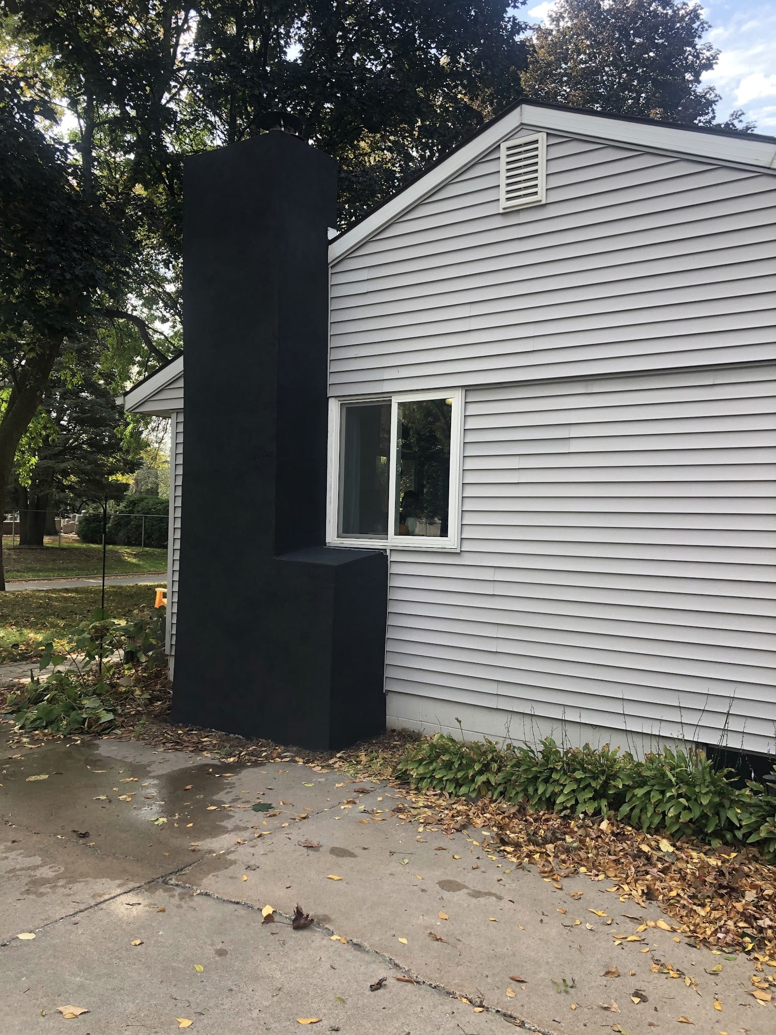Black stucco chimney on gray vinyl-sided house exterior.