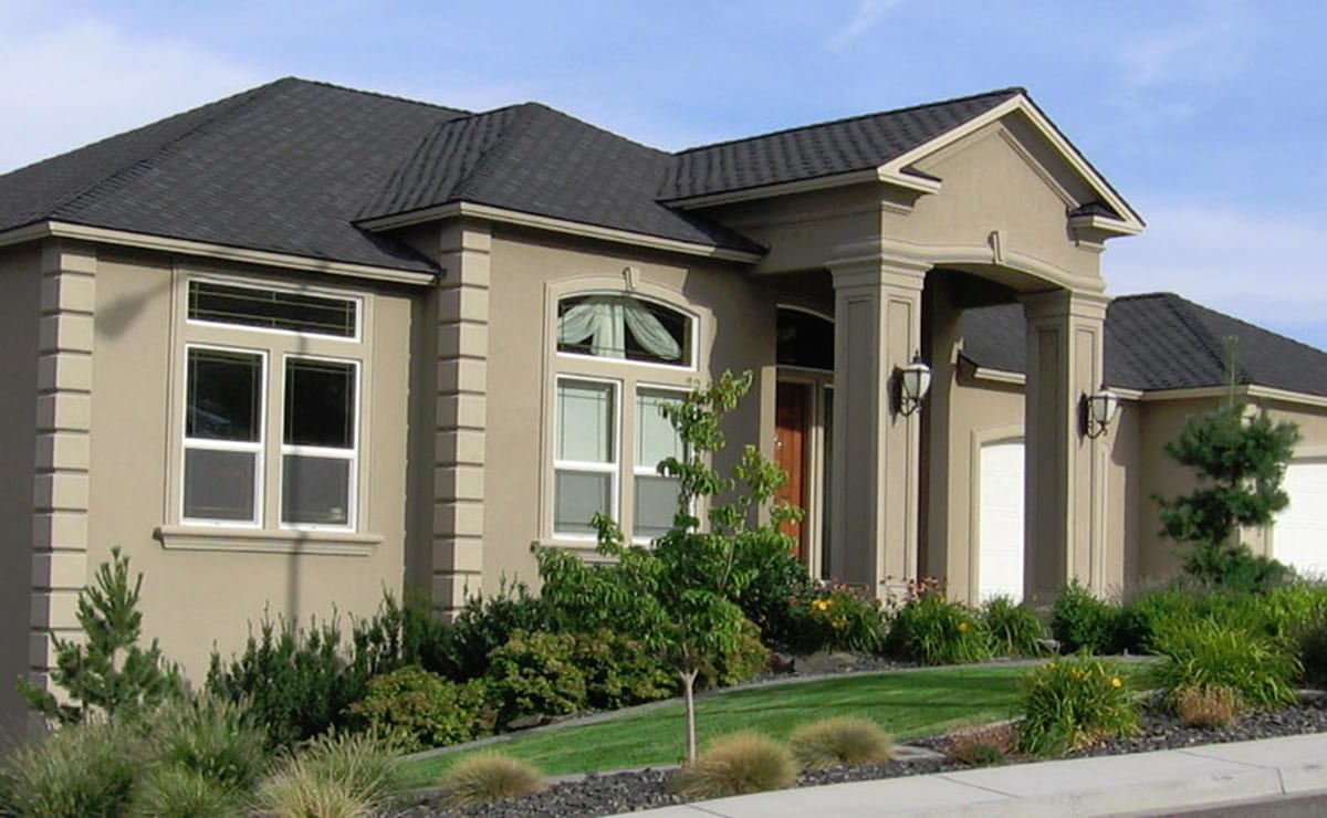 Tan stucco exterior home with dark roof and landscaped front yard