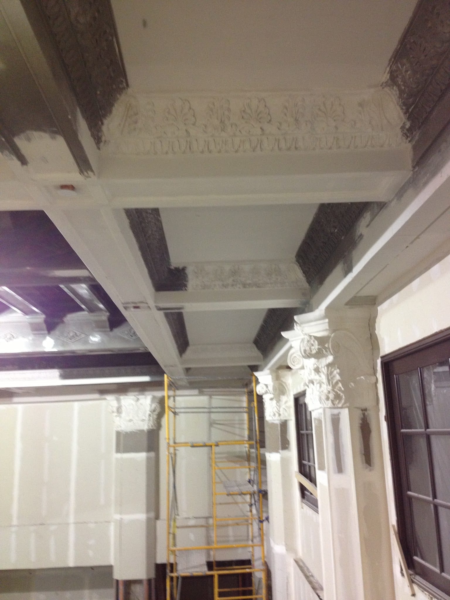 Ornate plaster ceiling and Corinthian columns under restoration with scaffolding