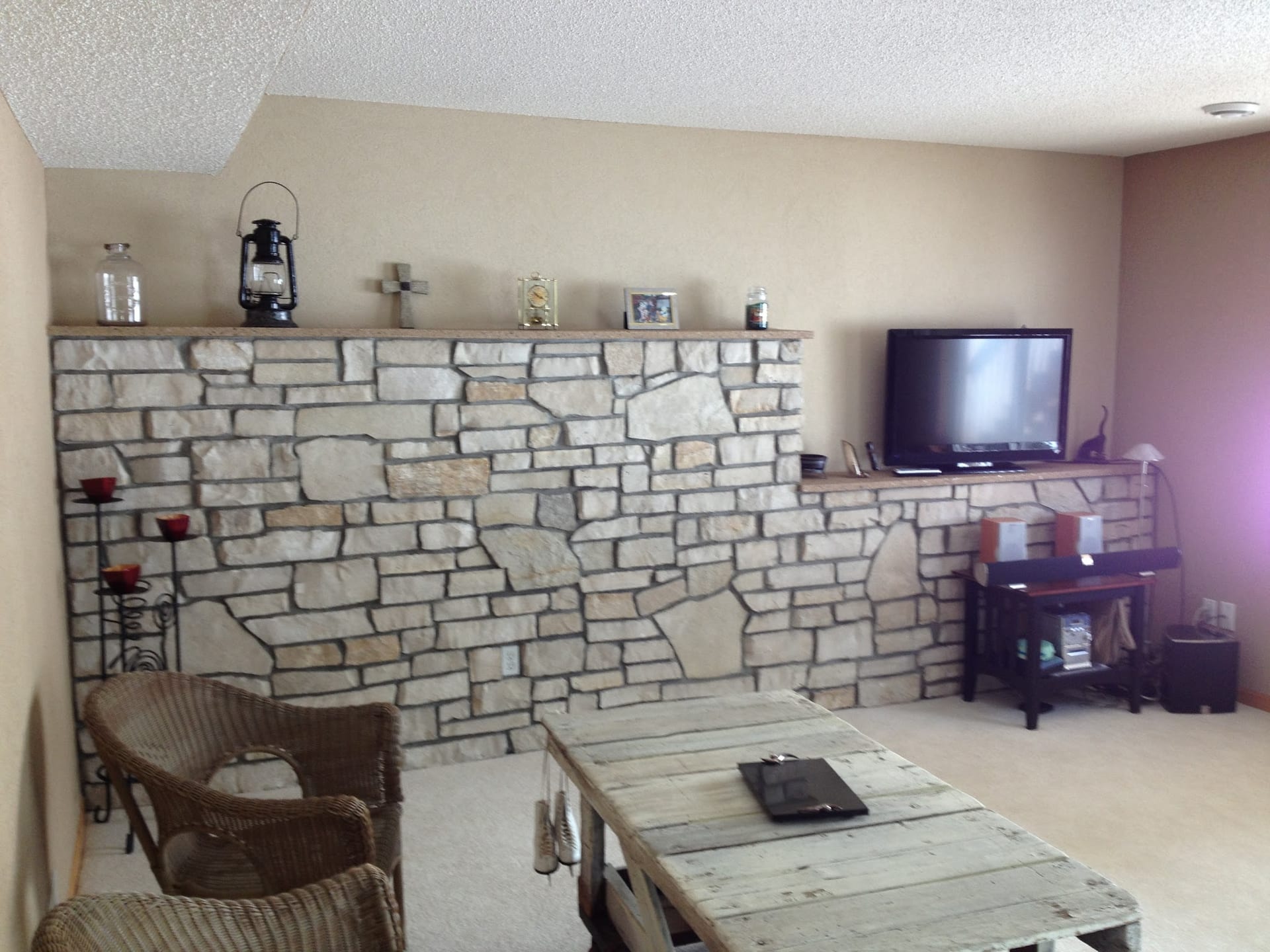 Stone accent wall with wooden shelf, candle holders, and TV in living room