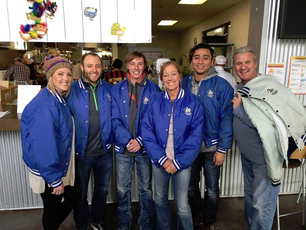 Six McClellan Stucco team members in blue jackets at a community event