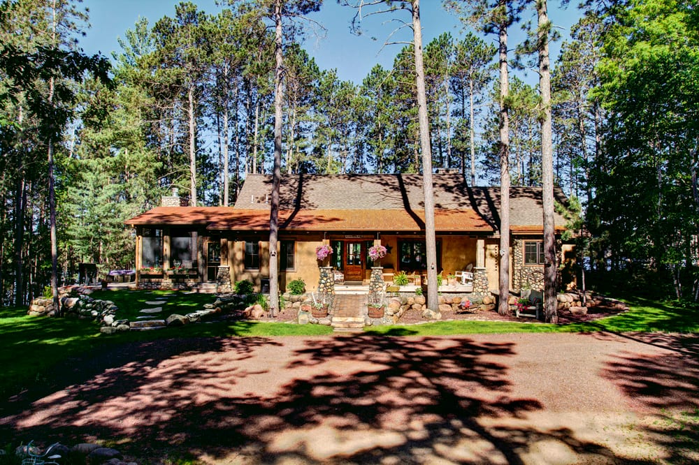Stucco exterior home surrounded by tall pine trees with stone accents