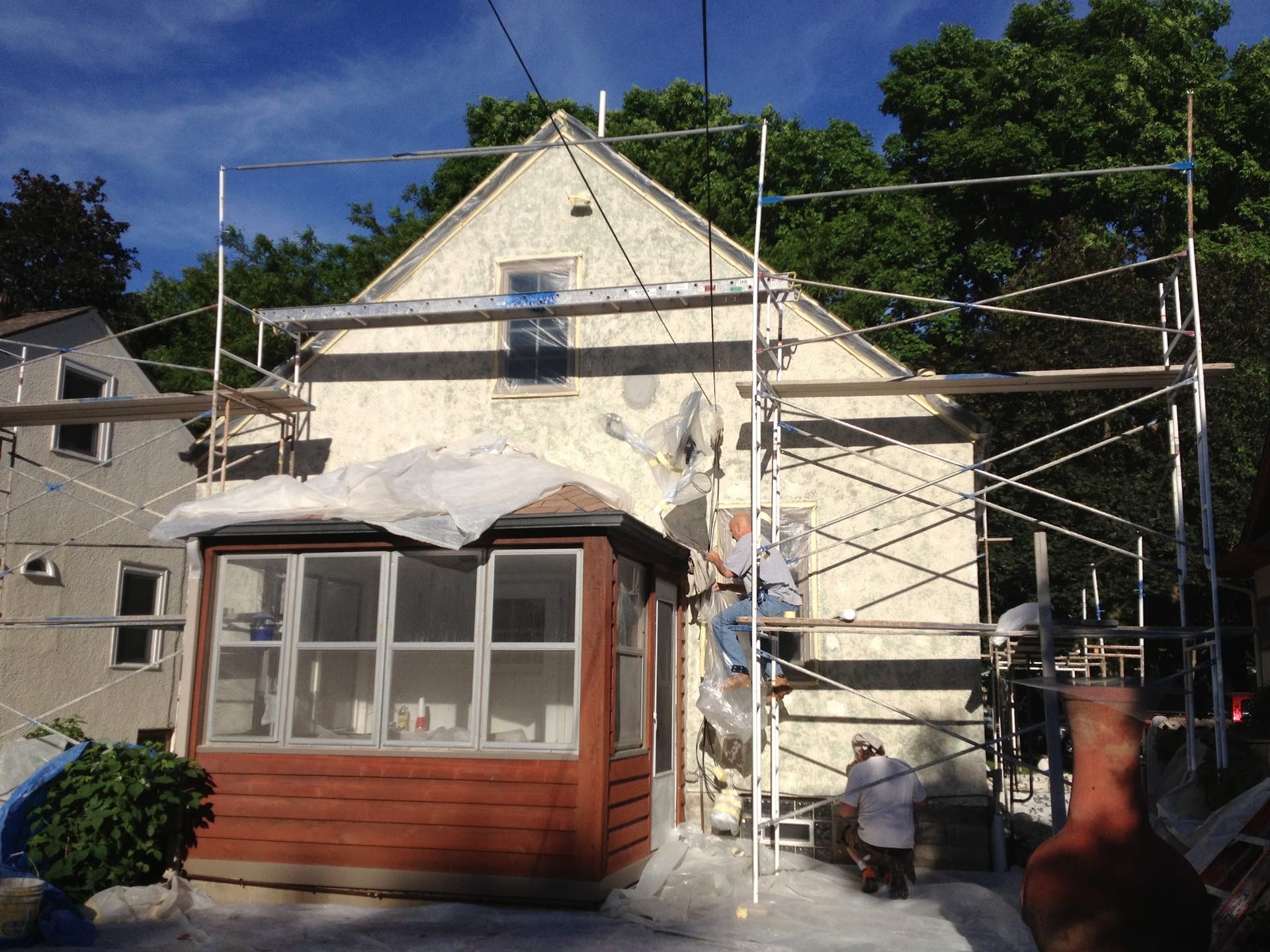 Workers on scaffolding applying stucco to a two-story home exterior