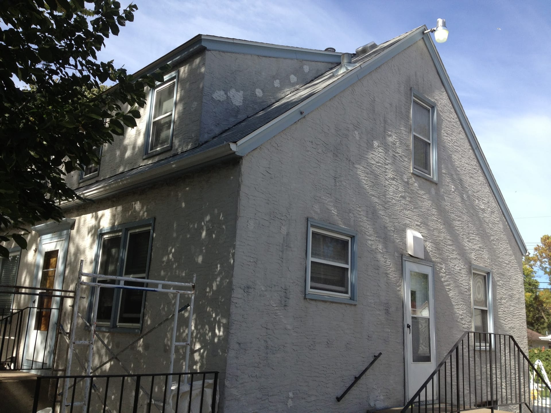 Two-story stucco home with visible patch repairs and scaffolding