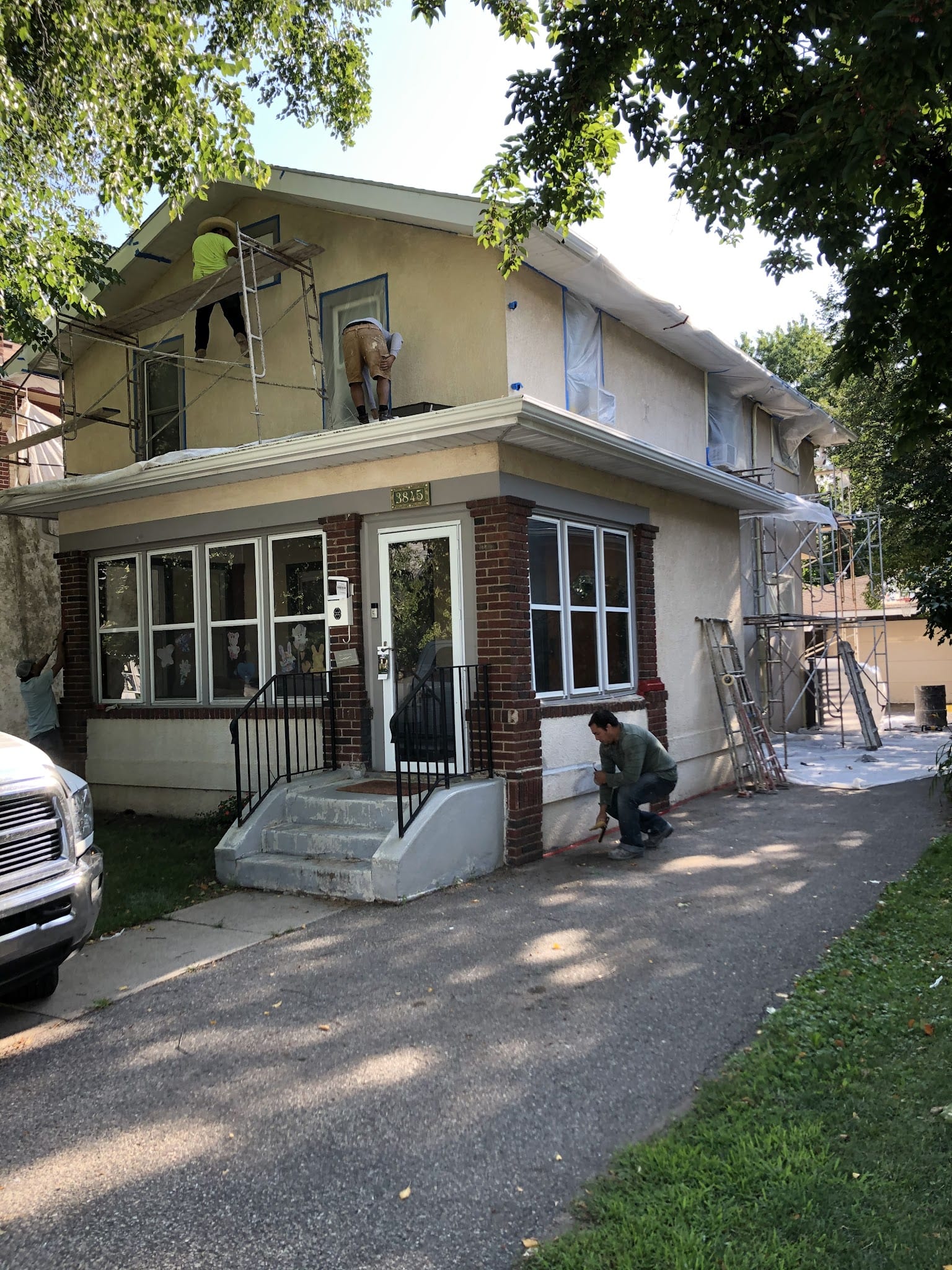 Workers on scaffolding repairing stucco exterior of two-story brick home.