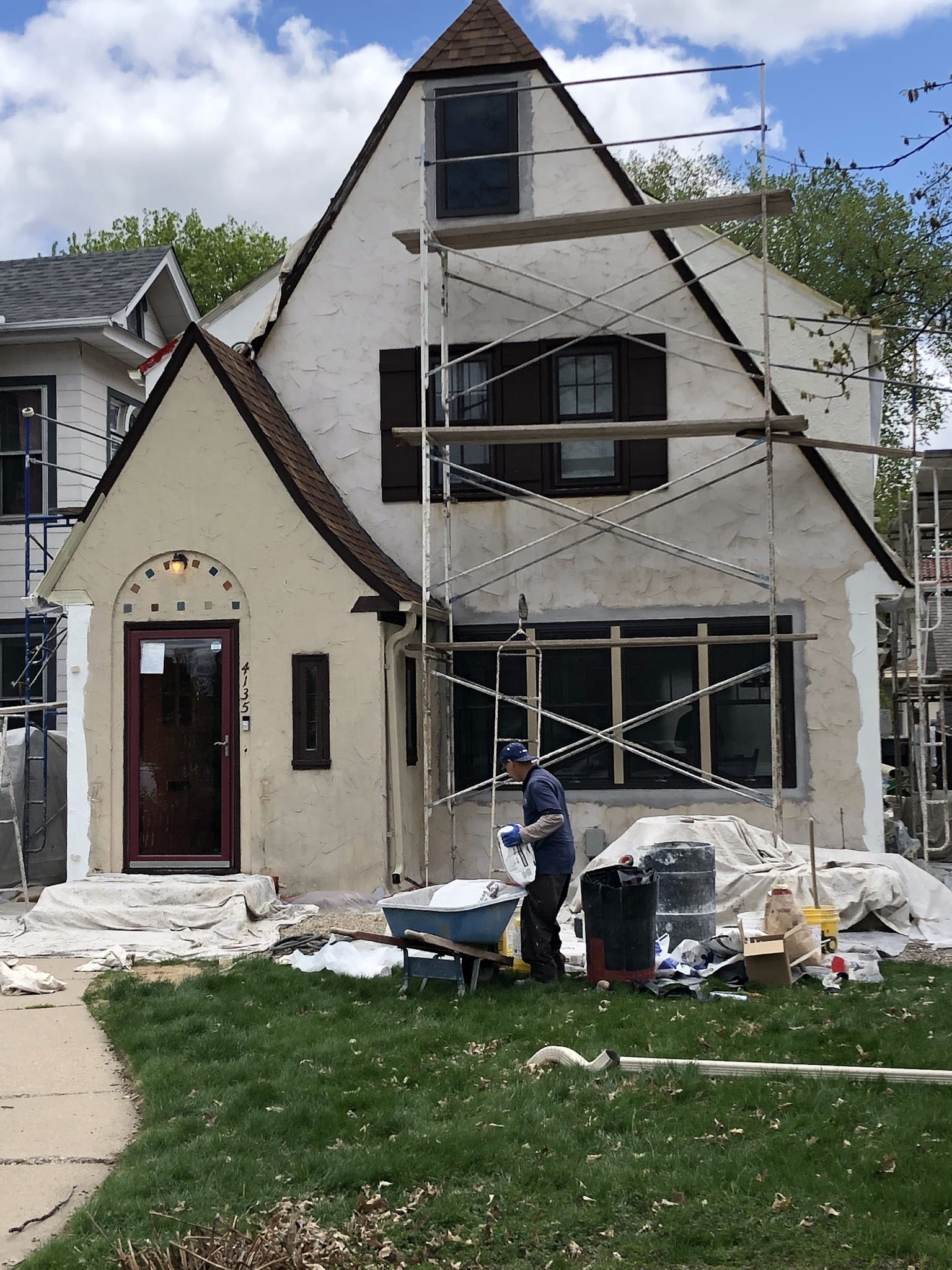 Worker mixing stucco beside scaffolding on a Tudor-style home exterior