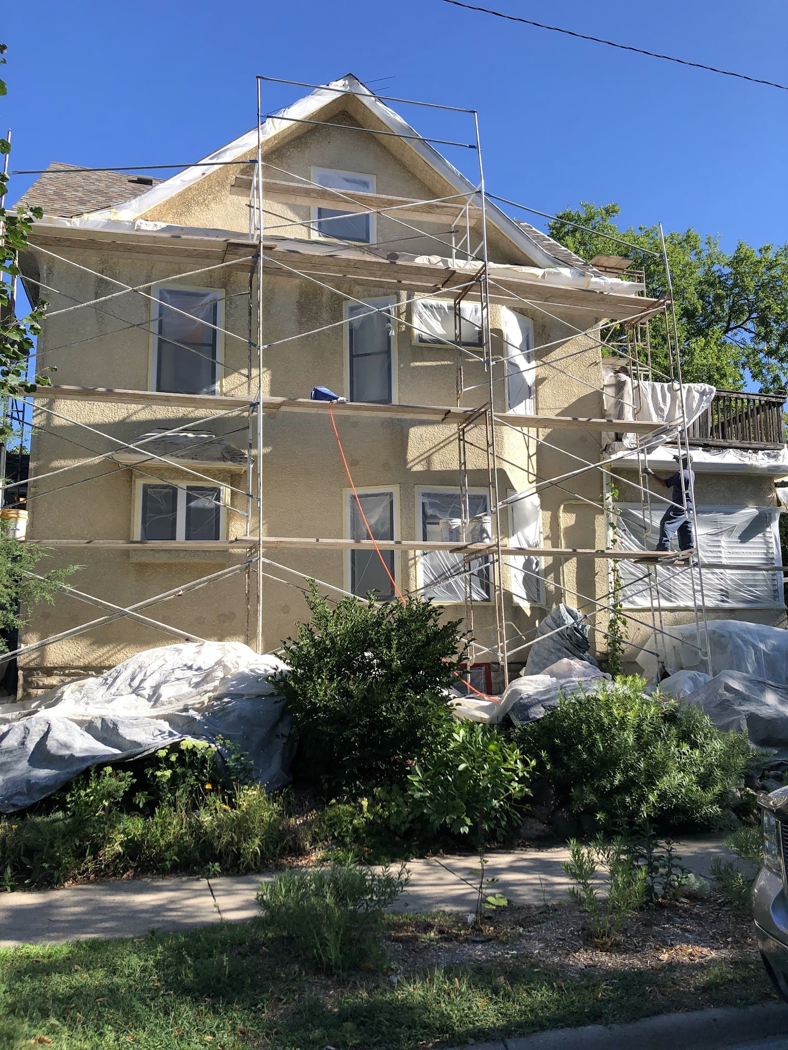 Three-story stucco home covered in scaffolding during exterior resurfacing work.