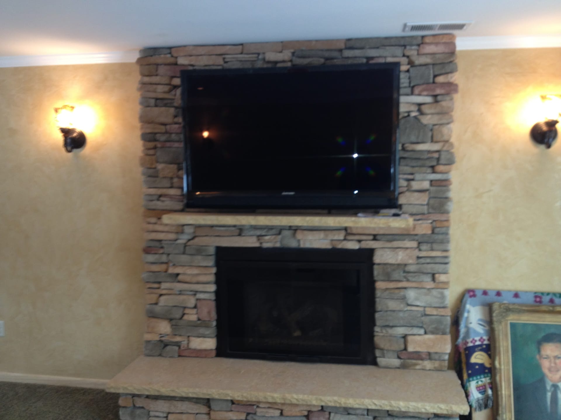 Stone fireplace with mounted TV and smooth plaster walls with sconces
